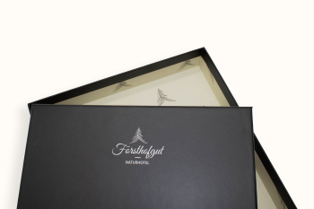 Boîte cadeau noire avec le logo de l’hôtel nature Forsthofgut et couvercle ouvert