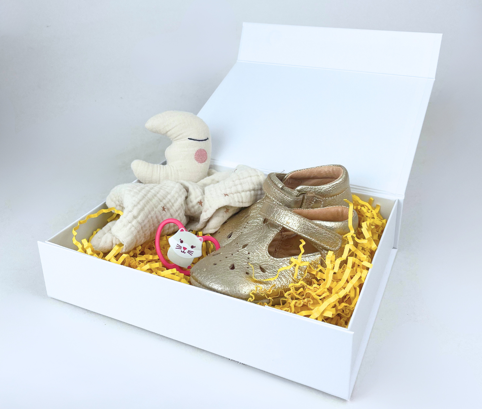 Boîte cadeau blanche avec chaussures de bébé, peluche et papier de calage jaune