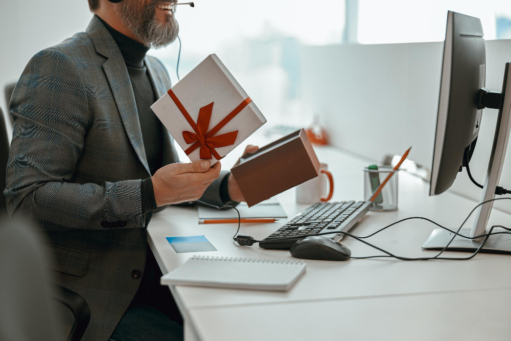 Homme au bureau vérifiant une boîte cadeau avec un nœud rouge pour des cadeaux d'entreprise.