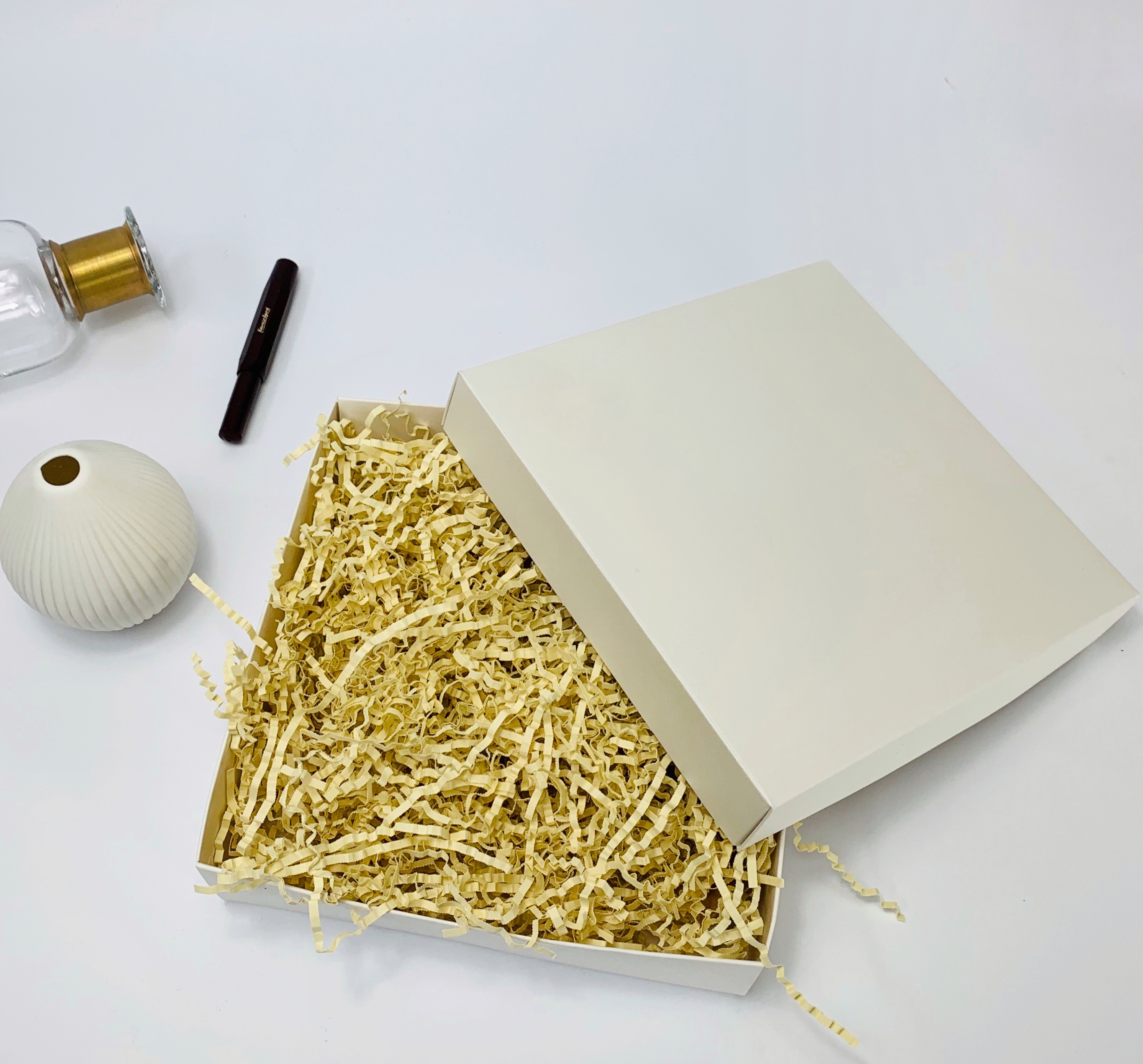 Boîte magnétique blanche avec matériau de remplissage à côté d'un vase et d'un stylo