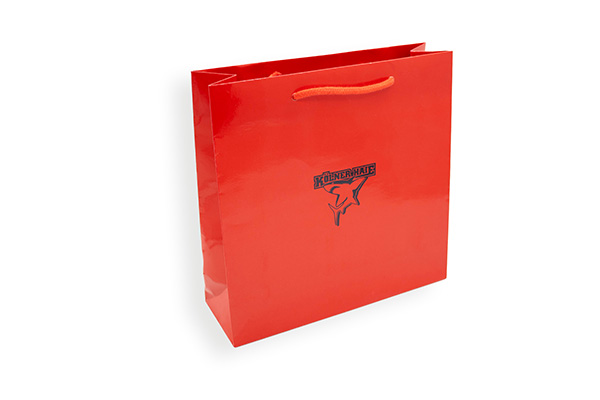 Sac en papier rouge brillant avec poignée en cordelette et logo des Kölner Haie